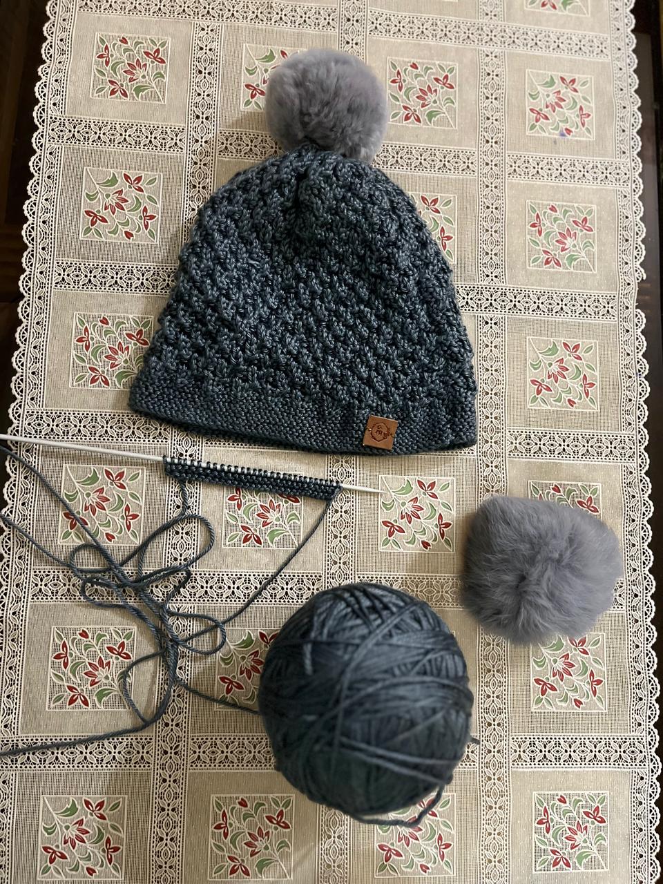 Chem Taas Heather Grey pom-pom beanie flat lay with knitting yarn