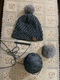 Chem Taas Heather Grey pom-pom beanie flat lay with knitting yarn
